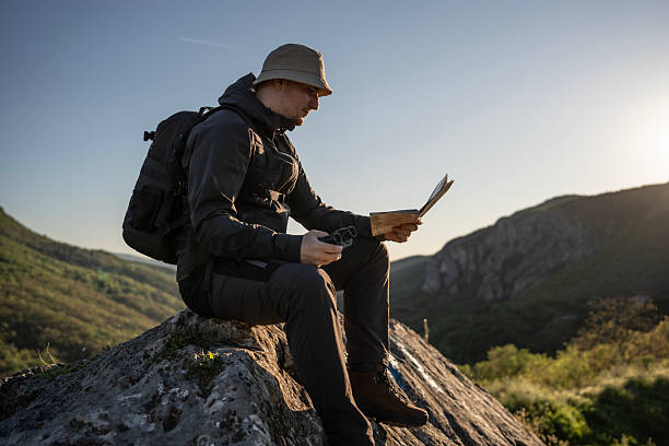 istock Explorer Relaxing on Rock with Map and Binoculars in Hand 2212617075