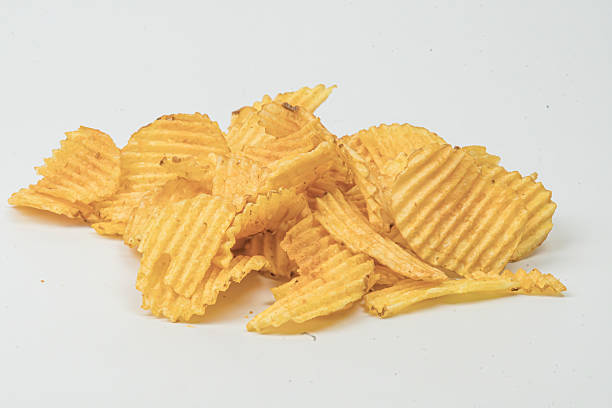 Close-up view of yellow, ridged potato chips on a light grey surface, with soft shadows.