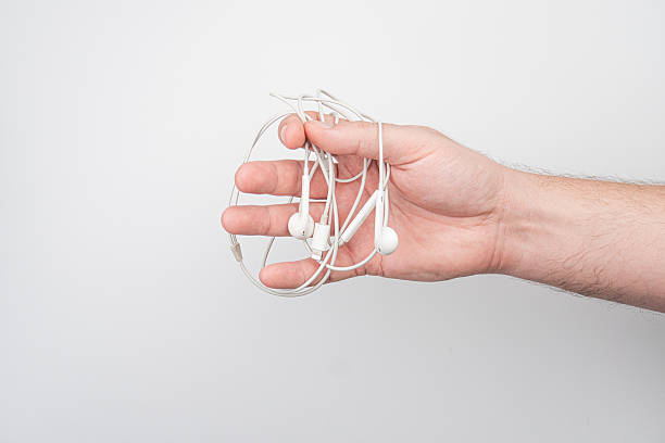 istock A hand holding a pair of tangled earbuds sits on a light-colored, nondescript surface under even lighting. 2212624359