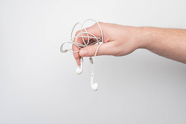 Relaxed hand holding tangled white earbuds, indoors with soft lighting and shadows on a wall Shallow depth of field, isolating and simplistic composition