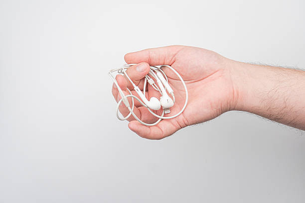 istock Hand releasing twisted gray cord white earbuds, blurred background, even lighting, muted colors. 2212624427