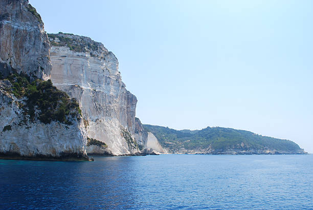Massive coastal cliffs with greenery rising above clear blue sea under bright sky, peaceful natural seascape on a sunny day concept of travel