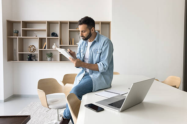 istock Young man remote worker reviewing paper documents at home office 2212628390
