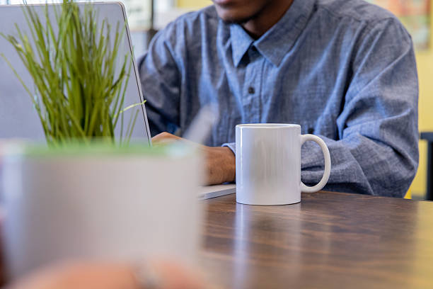 Gen Z professional man sips coffee while using laptop in modern coworking space