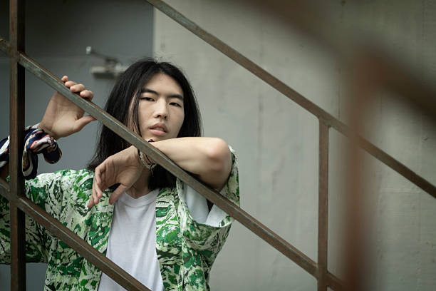 Portrait of a fashionable young man with long hair leaning on a railing, looking at the camera