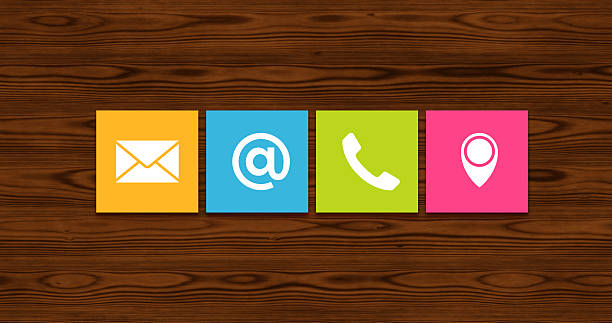 Colorful sticky notes displaying contact method icons (email, website/@, phone, location pin) pinned on a wood texture background. Represents providing contact information, customer service options, and various communication channels.