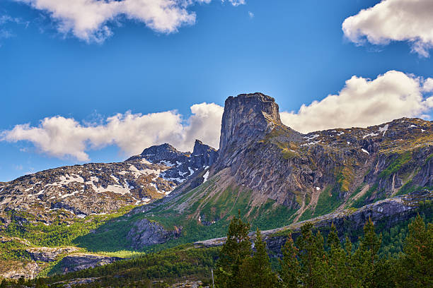 A stunning depiction of a rugged mountain landscape in Norway. The scene features towering peaks, patches of greenery, and a clear blue sky dotted with fluffy clouds, showcasing the untouched beauty of nature.