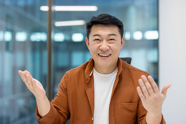 istock Webcam view, successful Asian man looking at camera smiling and communicating with colleagues and partners. Online business meeting, conference presentation, businessman sitting at desk inside office 2212638840