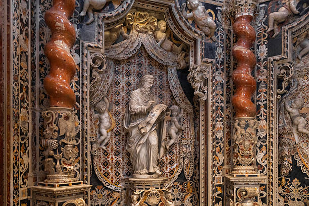 Monreale, Italy - July, 25, 2024: detailed view of ornate statue set within intricately decorated alcove in cathedral, featuring marble columns and cherubs
