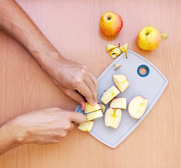 istock Overhead view of hands slicing apples on a cutting board. Fresh fruit preparation. Ideal for food, health, or lifestyle content. Natural light, warm tones. 2212650145
