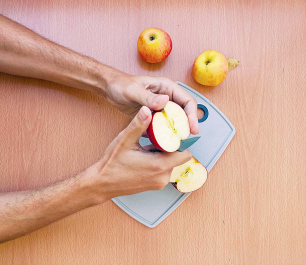 istock Hands cutting a fresh apple with a knife on a board. Healthy eating, snack preparation. Bright, overhead shot. Food blog, recipe, or lifestyle concept. 2212650197