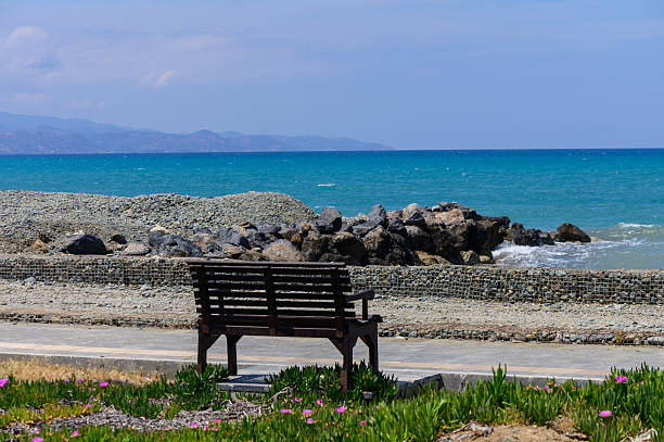Wooden bench facing the sea at sunset on Cyprus island. Peaceful landscape, warm Mediterranean colors, romantic atmosphere, perfect spot for relaxing and enjoying nature