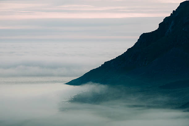 Mountain slope vanishes into dense coastal fog at dusk. in Unstad, Nordland, Norway