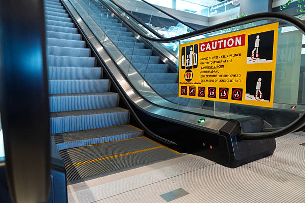 Close-up of an escalator in a shopping mall with a prominent yellow safety sign advising users on proper riding etiquette and cautionary rules.