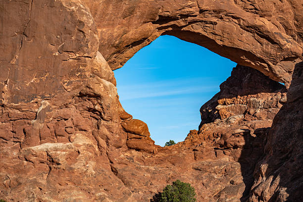 The stunning Skyline Arch in Arches National Park, Utah, stands tall against a brilliant blue sky. This magnificent sandstone formation, shaped by millennia of erosion, is a highlight of the park’s red rock landscape. Surrounded by desert vegetation and rugged terrain, it offers an awe-inspiring scene for hikers, photographers, and nature lovers exploring the beauty of the American Southwest.