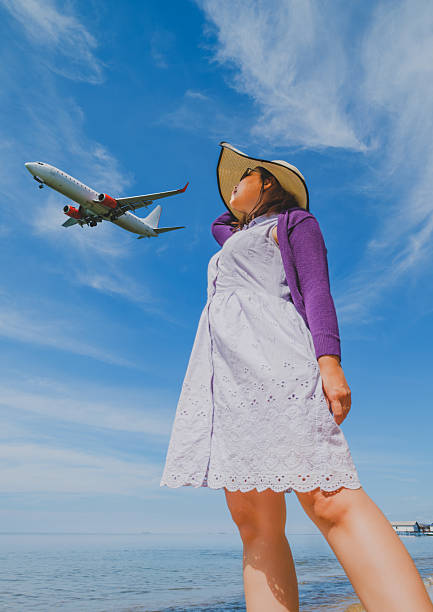 the woman is watching the airplane passing by near the beach. this photo concept suitable for travel theme.