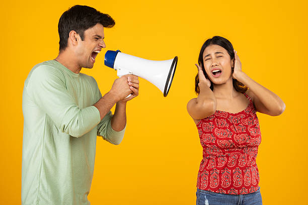 istock Man shouting with megaphone at his girlfriend on yellow background 2212680167