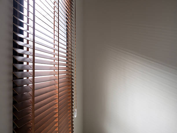 istock Image of brown wooden window blinds ropes being pulled open to allow sunlight into the room, casting light and shadow, overlay patterns on empty blank white wall background with copy space, nobody. 2212680304