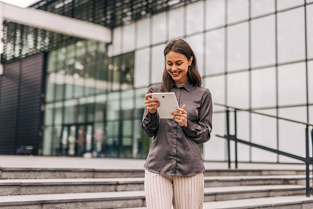 istock Smiling businesswoman using digital tablet in front of office building 2212680400