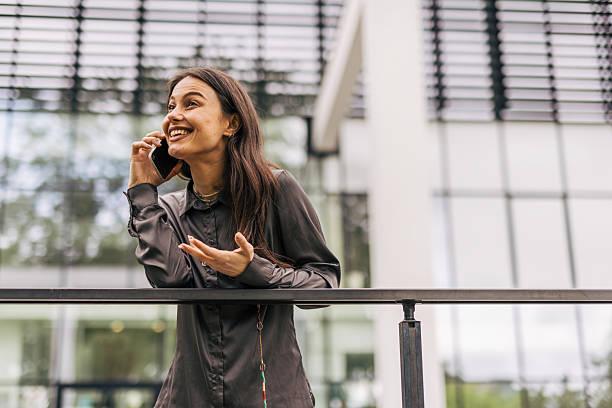 istock Businesswoman leaning on railing while talking on phone outside office building 2212681134