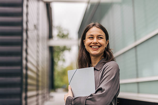istock Young businesswoman smiling and holding documents in urban setting 2212682338