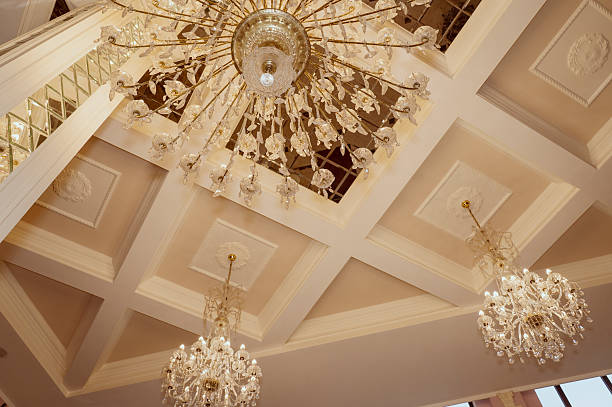 Three crystal chandeliers on the ceiling, view from below. In the center is a huge one and two smaller ones. Luxurious crystal chandeliers with gold elements and hanging glass pendants, rounded shape.