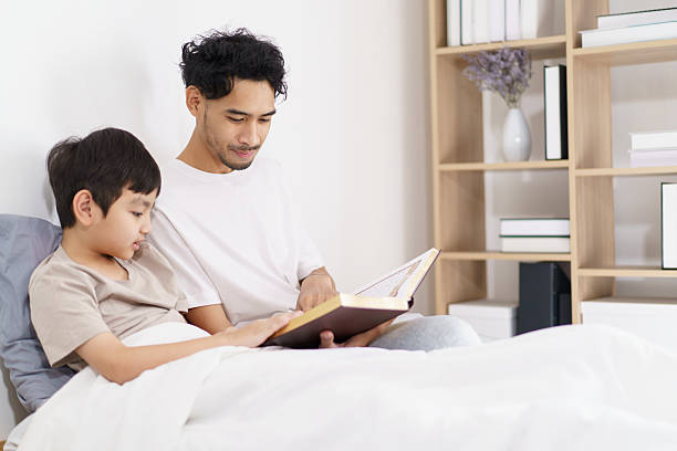 istock A man and son sitting on the bed together, meanwhile, reading a book. 2212684950