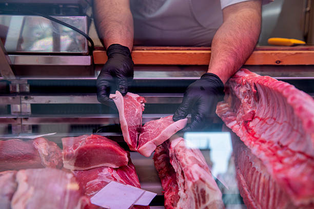 istock Butcher arranging fresh pork cuts in display case 2212688234