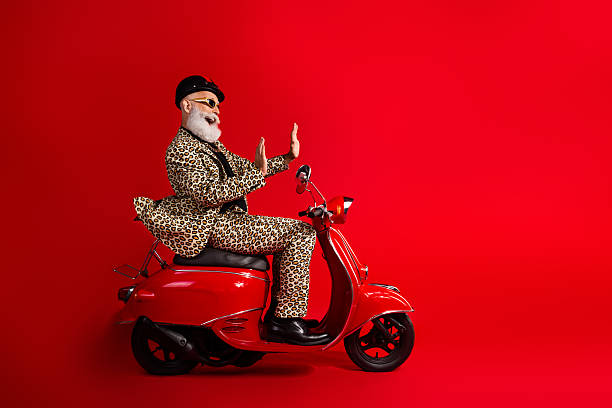 istock Glamorous elderly man in leopard-print suit on red scooter showing playful gestures over a vibrant red background 2212691109
