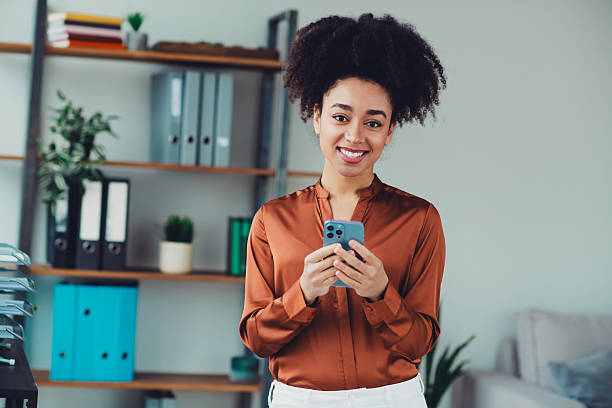 istock Confident young businesswoman holding a smartphone while standing in a modern office with organized interiors and stylish decor 2212693437