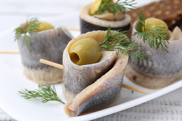 Delicious herring rolls with olives and dill on table, closeup