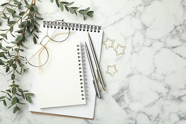 istock Paper clips, notebooks, pens, glasses and green branches on white marble table, flat lay. Space for text 2212694579