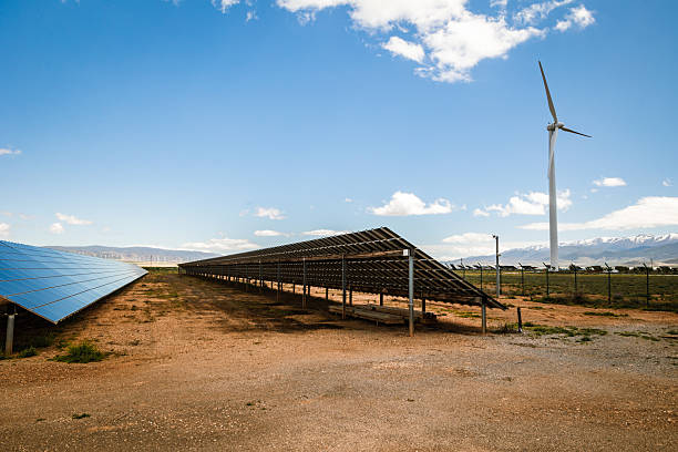 istock Hybrid renewable energy site with solar panel rows and wind turbine on dry terrain under clear sky near mountains 2212695141