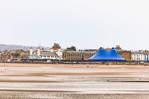 A wide shot of the Low Green in Ayr, Scotland, featuring a large blue marquee for the Pavilion Festival in May 2025. The scene includes the beach, town, and overcast sky.