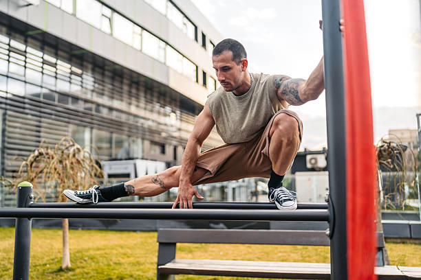 A handsome young man stretching before a workout outdoors on a gym bar in an outdoor gym.