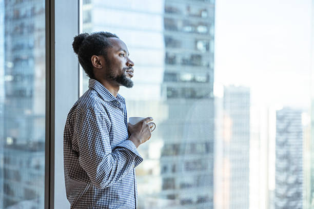 istock Thoughtful Individual Relaxing with Coffee at the Panoramic Window Enjoying the View on a Modern Cityscape 2212701356