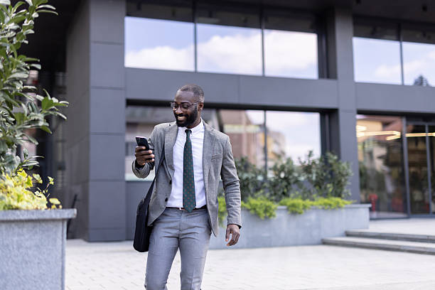 istock Stylish man smiling while walking with smartphone outdoors 2212704321