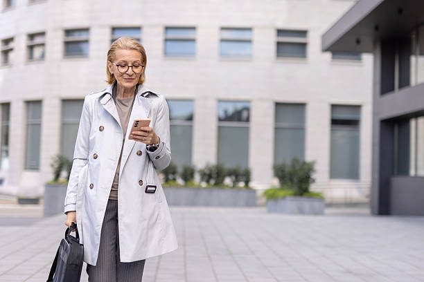 istock Woman in stylish trench coat using her smartphone outside 2212704322