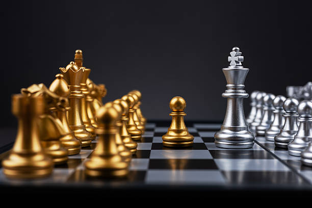 istock King silver chess standing confront of the golden chess team. 2212705970