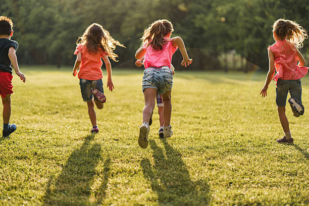 Rear view of group of carefree children running on a meadow during summer day