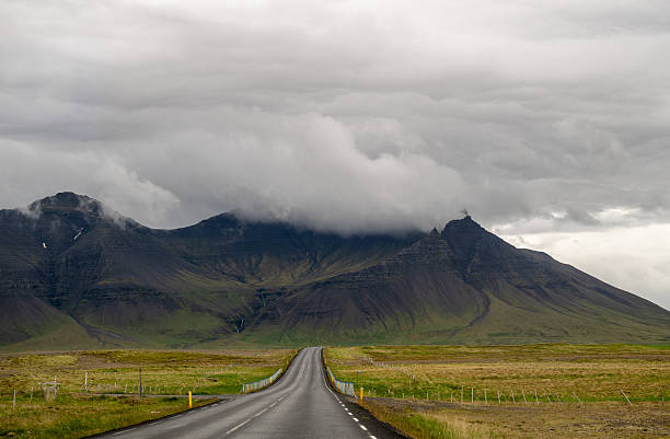 Empty road leading to misty mountain range under dramatic cloudy sky in Iceland