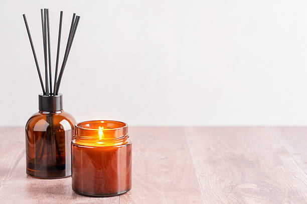 istock Aromatherapy setup with scented glowing candle and reed diffuser in brown glass bottle on table with copy space 2212713645