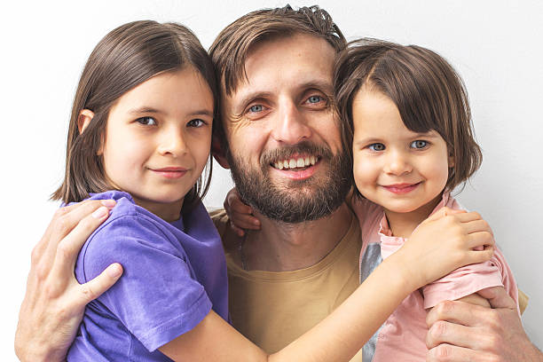 istock Happy bearded father in his 30s hugging his two smiling daughters aged 3-4 and 7-8 in front of white background concept of parenthood and love 2212715475