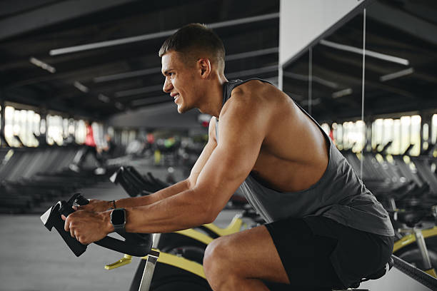 istock Side view of handsome man exercising on stationary cycle in modern gym while holding handle bar 2212722374