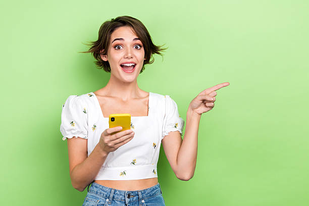 istock Photo of impressed excited woman dressed white texting modern gadget pointing empty space isolated green color background 2212723969