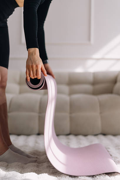 istock Woman rolls up a yoga mat after completing a home workout session 2212724293