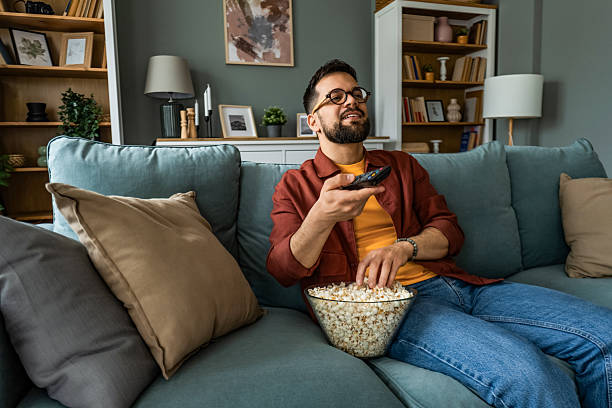 istock Young man relaxing at home and watching TV 2212725532