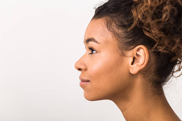 Young Woman With Curly Hair Poses Sideways Against a Plain Background