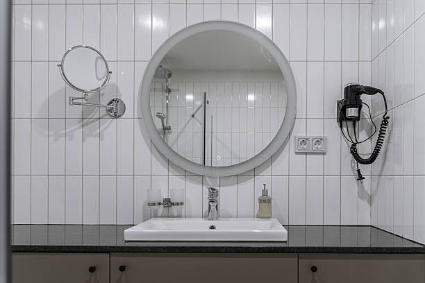 istock bathroom design with white tiles, white sink, gray bedside table under the sink, large and small round mirrors, hairdryer. 2212727813