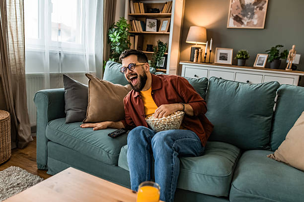 istock Young man watching TV at home and laughing 2212728402